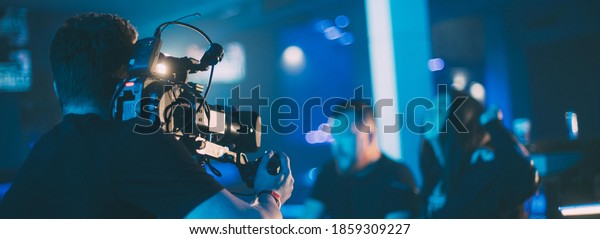 Director\
of photography with a camera in his hands on the set. Professional\
videographer at work on filming a movie, commercial or TV series.\
The filming process indoors, on a concert\
stage.