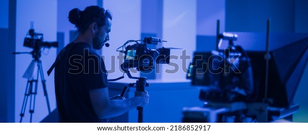 Director of photography
with a camera in his hands on the set. Professional videographer at
work on filming a movie, commercial or TV series. Filming process
indoors, studio