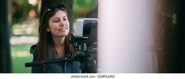 The director of photography is a woman behind a video camera on the set. A professional videographer at work on the filming of a movie, commercial or TV series. Filming process indoors, studio - Shutterstock ID 2208916303