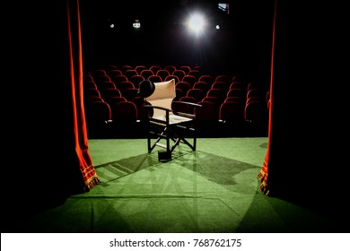 Director's chair on stage, in front of empty seats and in between curtains - Powered by Shutterstock