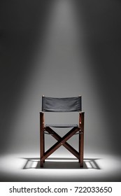 A Directors Chair Sits Against A Plain Dark Background Illuminated By A Single Overhead Spotlight.