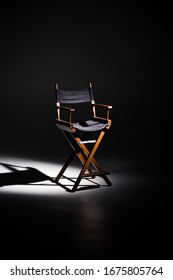 Directors chair stands in the beam of light. Space for text.
Vacant chair. The concept of selection and casting. Shadow and light.