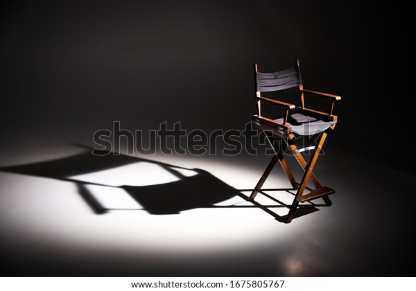 Directors chair stands in the beam of light. Space\
for text.\
Vacant chair. The concept of selection and casting.\
Shadow and light.