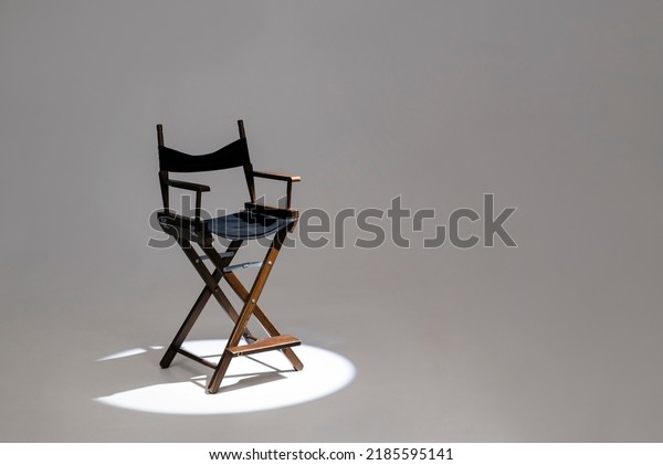 Directors chair stands in the beam of light. Space\
for text. Vacant chair. The concept of selection and casting.\
Shadow and light.