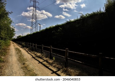 Dirt Path Partly In The Shade Casted By A Hedge And Split By A Wooden Fence In The Countryside