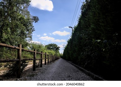 Dirt Path Partly In The Shade Casted By A Hedge And Split By A Wooden Fence In The Countryside