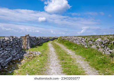 A dirt path with stone walls and a gate on a bright sunny day with a blue sky at Inishmore island, Galway - Shutterstock ID 2343201077
