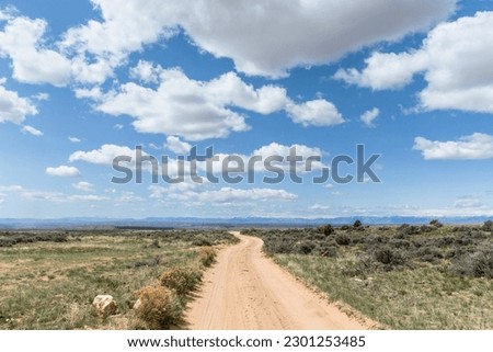Dirt road in the country leading to a beautiful scenic landscape of mountains in the distance using shallow depth of field on a partly cloudy day with cumulus clouds in the blue sky