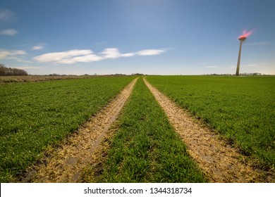 Dirt Road In The Field Leading To The Wind Turbines.