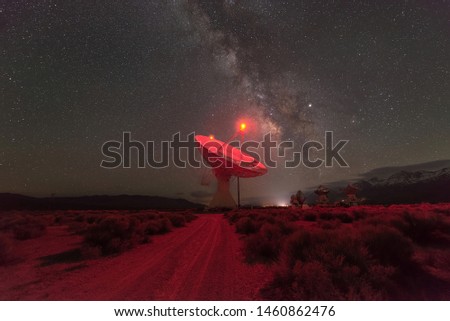 Dirt road leading towards a large radio dish antenna at night with the Milky Way Galaxy visible 