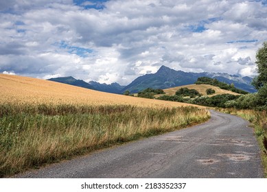 a dirt road next to a grain field heading into the high mountains. Kriváň in the High Tatras stands out in the background.
