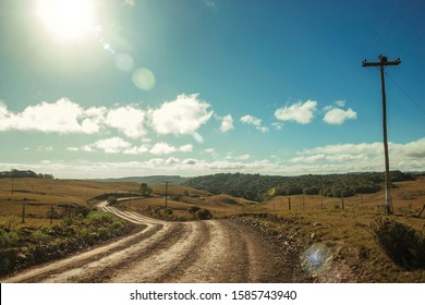 Dirt Road Passing Through Rural Lowlands Called Pampas With Hills And Sunlight Near Cambara Do Sul. A Small Country Town In Southern Brazil With Amazing Natural Tourist Attractions. Retouched Photo.