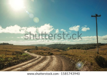 Dirt road passing through rural lowlands called Pampas with hills and sunlight near Cambara do Sul. A small country town in southern Brazil with amazing natural tourist attractions. Retouched photo.