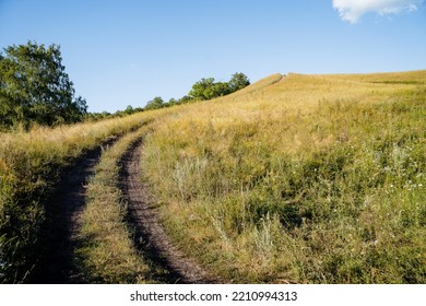 Dirt Road Steeply Rises Up The Field, Mountainous Terrain, Evening Landscape, Smooth Turn Of The Road, Horizon Line, At The Top Of The Mountain, Russian Field. High Quality Photo