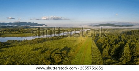 Dirt road through green rural landscape by river on misty morning