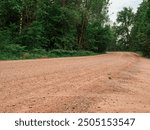 A dirt road with trees in the background. The road is empty and there is no one on it. Country side way without proper asphalt surface.