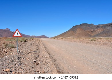 A dirt road in the vast sossusvlei desert in Namibia Southern Africa with mountains in the background and a sign alerting drivers of crossing oryx or gemsbock