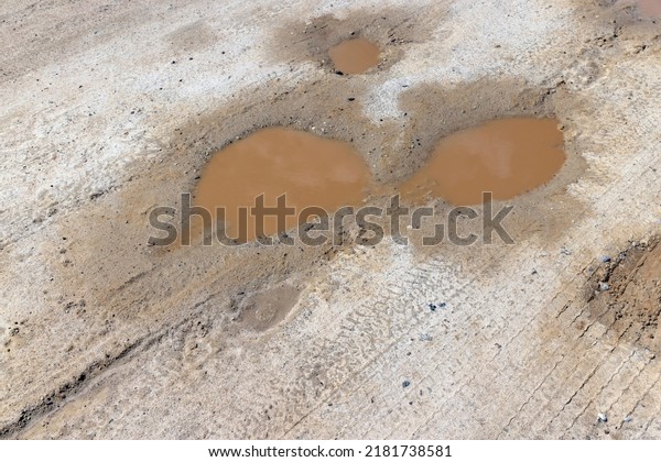a dirt road with a lot of water holes, puddles on a\
dirt road after rains