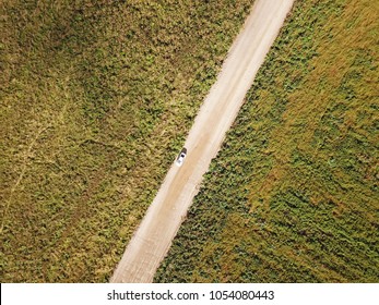 A Dirt Road With A White Car In A Field - A Top View In Autumn