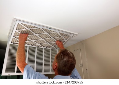 Dirty Air Filter Being Removed From A Home Furnace Air Intake Vent By An Adult White Male Close-up. Adult White Male Removing A Dirty Air Filter From A Furnace Air Duct Intake Vent In A Home Ceiling.