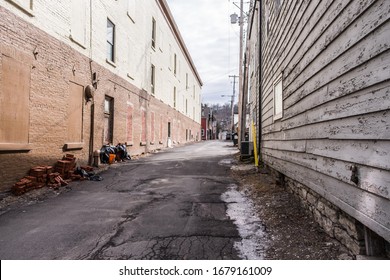 Dirty Alleyway In Downtown Hudson New York. Trash On The Side Of The Brick Building. Damp Pavement Along The Edges Of This Gritty Street.