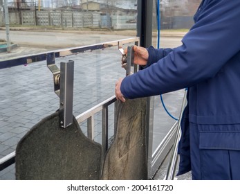 Dirty Auto Mat At A Self-service Car Wash. Cropped Photo Of A Man In Blue Jacket Hanging Car Mats With Steel Pegs For Cleaning In The Manual Self-service Washing Station.