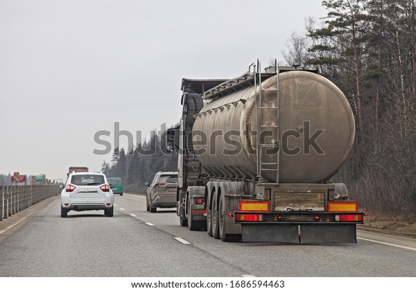 Dirty\
barrel fuel tank truck on suburban two-lane road at Spring day on\
forest background, liquid cargo\
transportation