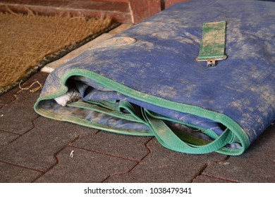 Dirty blue and green horse blanket laying on the floor of a stable