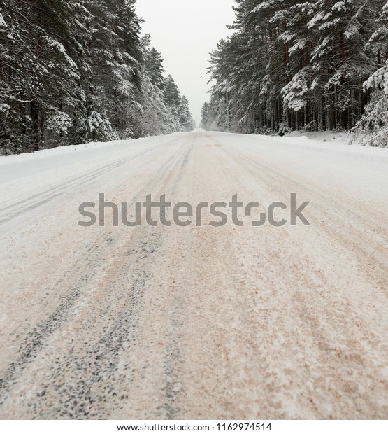 a dirty,\
broken snow covered road in the winter season, a road built through\
a coniferous forest, cloudy\
weather