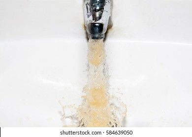 Dirty brown running water falling into a white sink from tap
