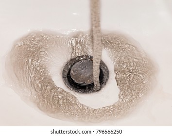 Dirty Brown Running Water Falling Into A Sink From Tap. Polluted Fresh Water