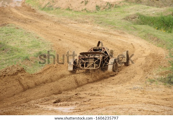Dirty buggy car on turn off road mud track, rear\
view on speed autocross\
racing