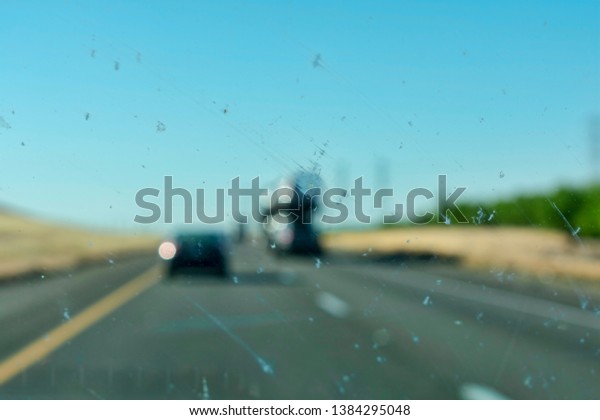 Dirty car window glass with insects and dirt affect\
driver visibility while driving on divided highway. The worn out or\
bad car wiper blades smear dead bugs and dirt all over windshield.\
