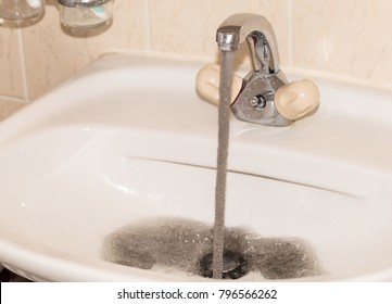 Dirty dark gray running water falling into a sink from tap. Polluted fresh water