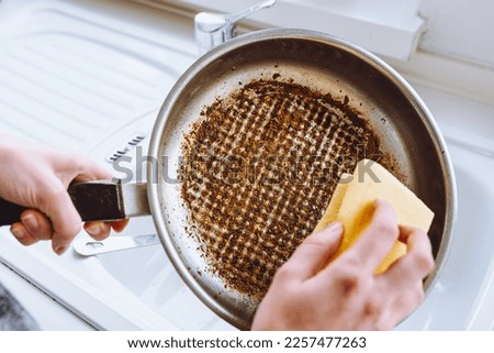 Dirty dishes with burnt food, household chores, washing dishes. woman's hand washes burnt greasy frying pan with kitchen washcloth in sink