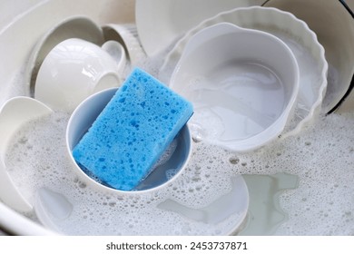 Dirty dishes with cleaning sponge in foam of dishwashing liquid. Washing dishes concept - Powered by Shutterstock