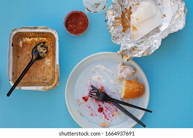 Dirty Disposable Tableware After A Meal Top View. A White Plastic Plate With Leftover Bread And An Aluminum Container With A Black Spoon. Leftover Food With Disposable Tableware On A Blank Background.