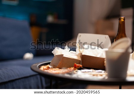 Dirty empty living room with food trash, bottle of beer and napkins on blue sofa. Unorganized house apartment of lonley woman with anxiety depresion having garbage, rubbish with no people in