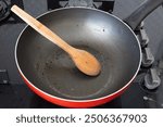 Dirty frying pan and wooden spoon on the stove. There are food and oil stains on the pan and wooden spoon. Cooking and dishes.