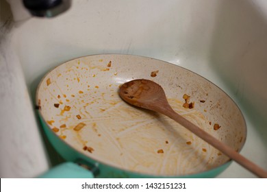 Dirty frying pan and wooden spoon in a sink - Powered by Shutterstock