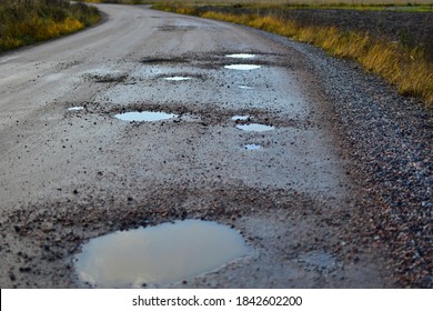 Dirty Gravel Road With Potholes. It Has Some Surface Damage, Needs Maintenance, Hole Patching, Dust Binding And Dragging. The Cost Of Maintaining Gravel Roads, Is Expensive And Time Consuming.