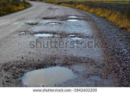 Dirty gravel road with potholes. It has some surface damage, needs maintenance, hole patching, dust binding and dragging. The cost of maintaining gravel roads, is expensive and time consuming. Stock photo © 