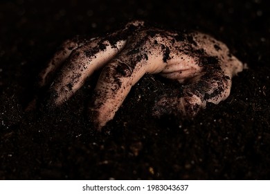 A dirty hand crawling out of the ground after being buried in a grave.  - Shutterstock ID 1983043637