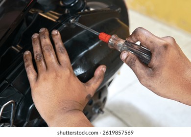 Dirty hands holding a screwdriver while tightening a part of a black motorcycle.