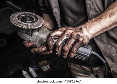 Dirty hands of mechanic holding angle grinder tool