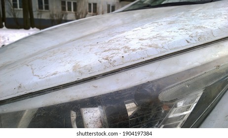 Dirty Headlight, Muddy Glass. Mud On White Hood Of Automobile. Car Wash In Snow. Washing The Body. Cleaning Vehicle. Corrosion Protection Concept. Safety Driving. Bodywork. Building Background.