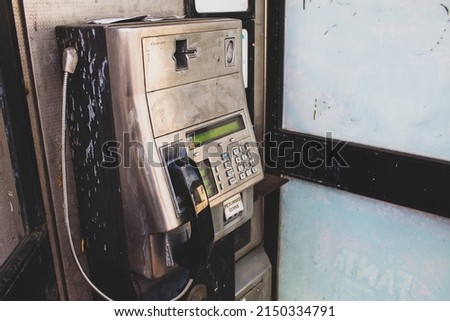 Dirty interior of a an English phonebox with coin slot, chargecard facility, metal keypad, digital display and black receiver with the receiver in focus and narrow depth of field