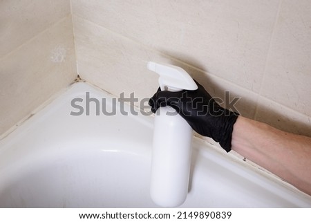 Dirty joints between the tiles, cleaning agent and hands in black gloves in the bathroom. Toxic black mold in the corner of the bathroom before cleaning.