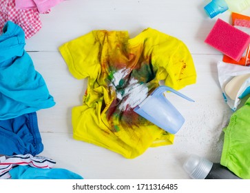 Dirty Kids Clothing Is Scattered On A White Wooden Table.Concept Of Searching For Information On Washing Spots, The Best Means For Cleaning Clothes.banner To Promote Advertising, Sales.