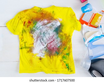 Dirty Kids Clothing Is Scattered On A White Wooden Table.Concept Of Searching For Information On Washing Spots, The Best Means For Cleaning Clothes.banner To Promote Advertising, Sales.